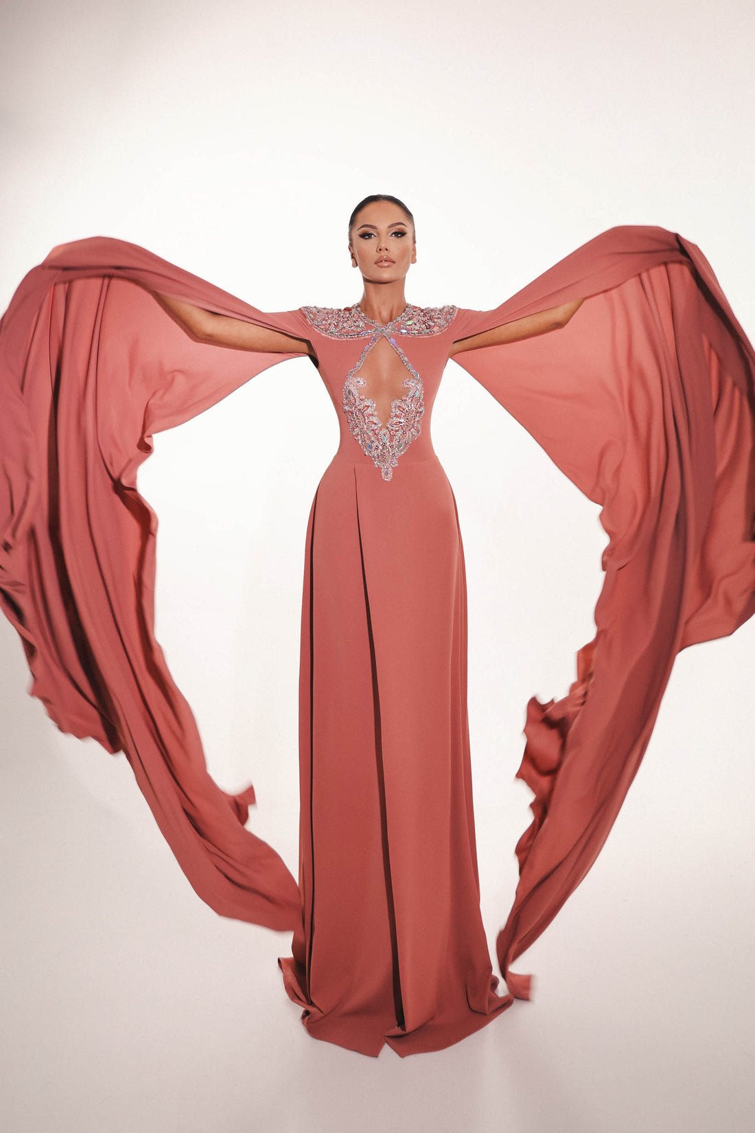 Blush couture gown with open cape sleeves in dramatic pose

