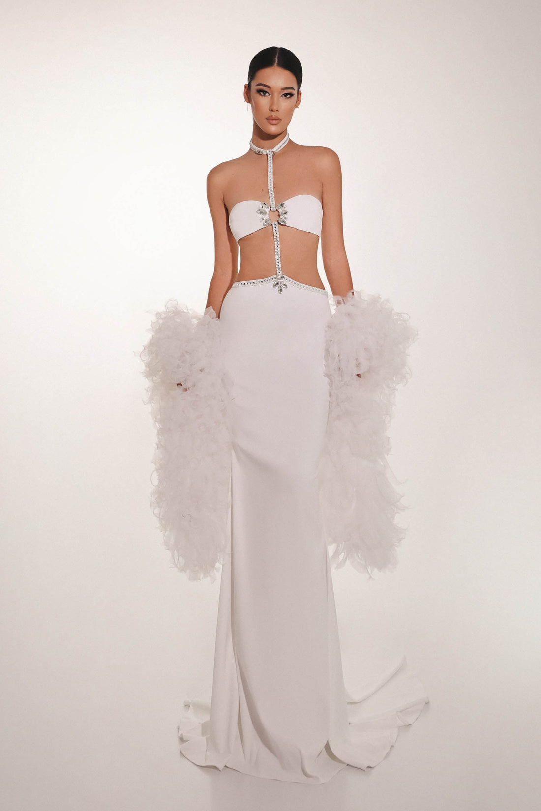 Model wearing a white outfit with feathered details on a plain background