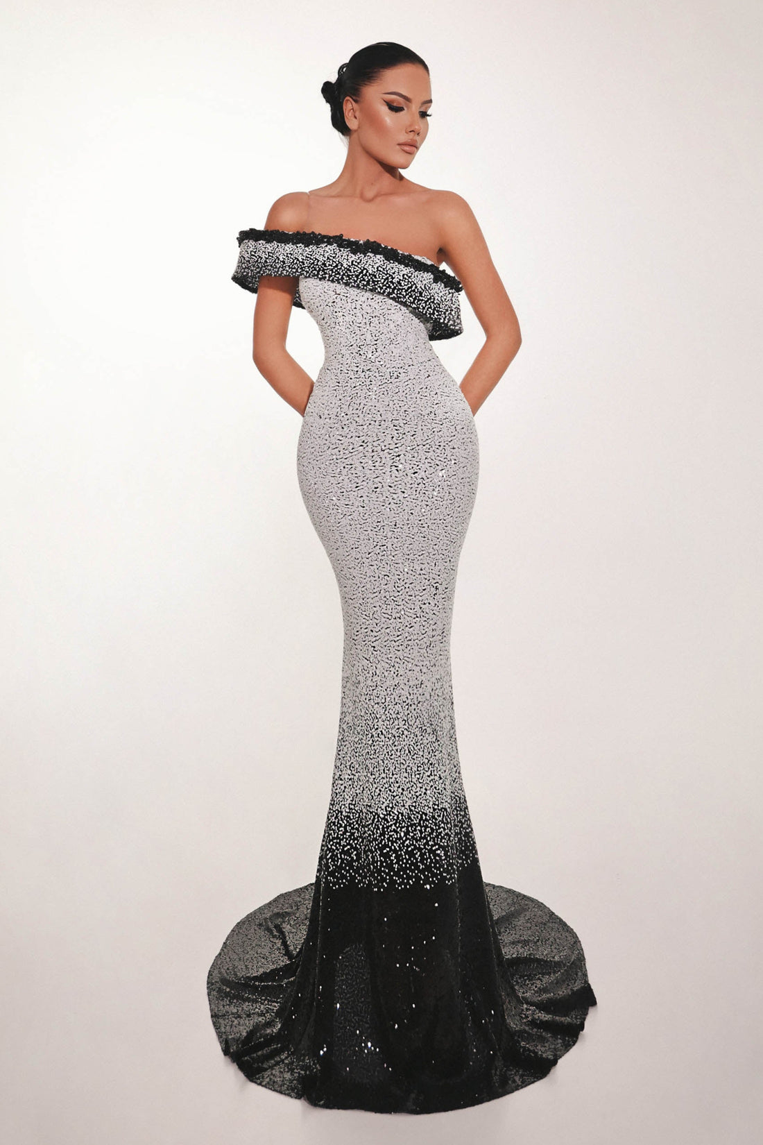 Woman wearing a black and white off-shoulder evening gown on a plain background