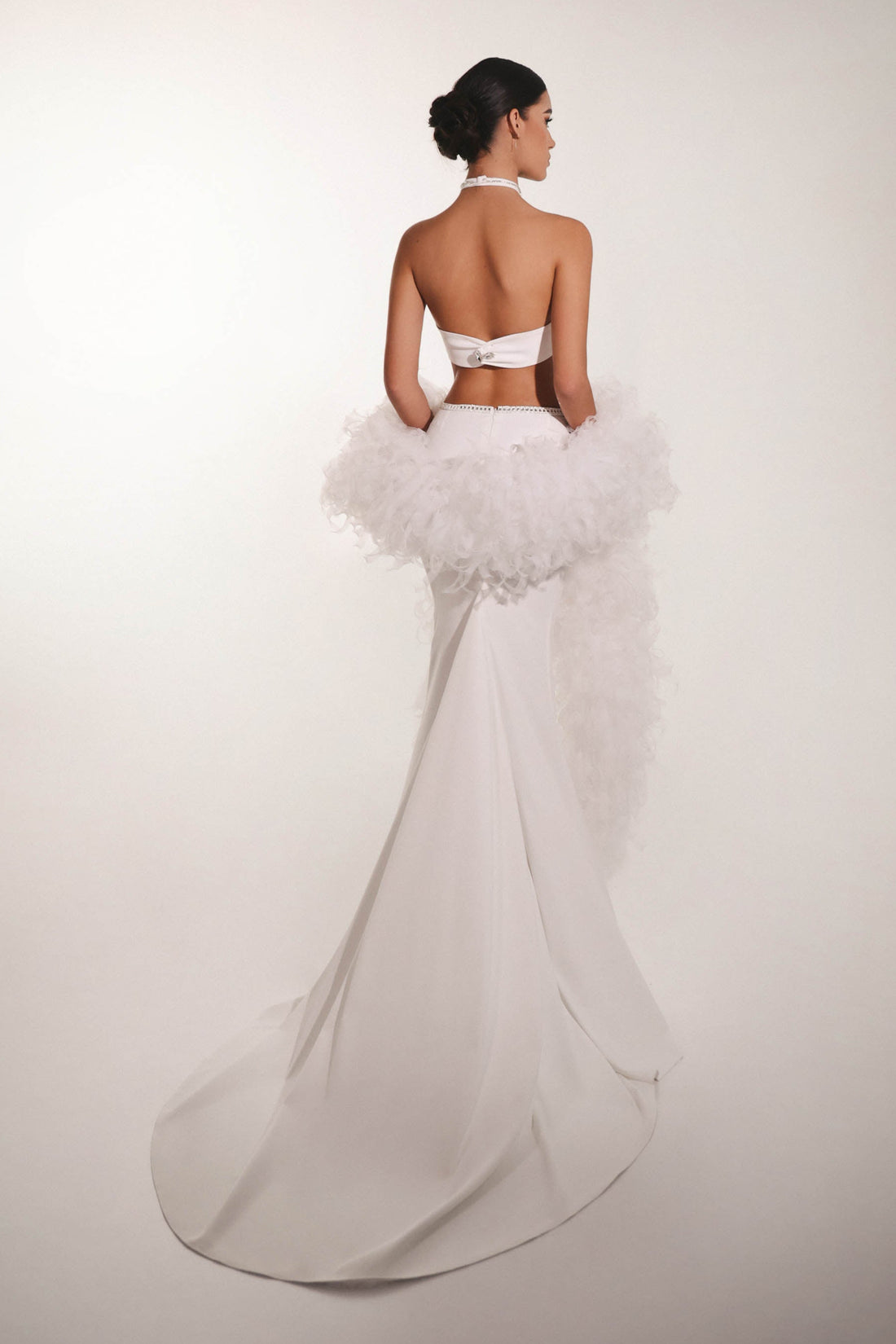 Woman wearing a white wedding dress with a ruffled skirt on a plain background