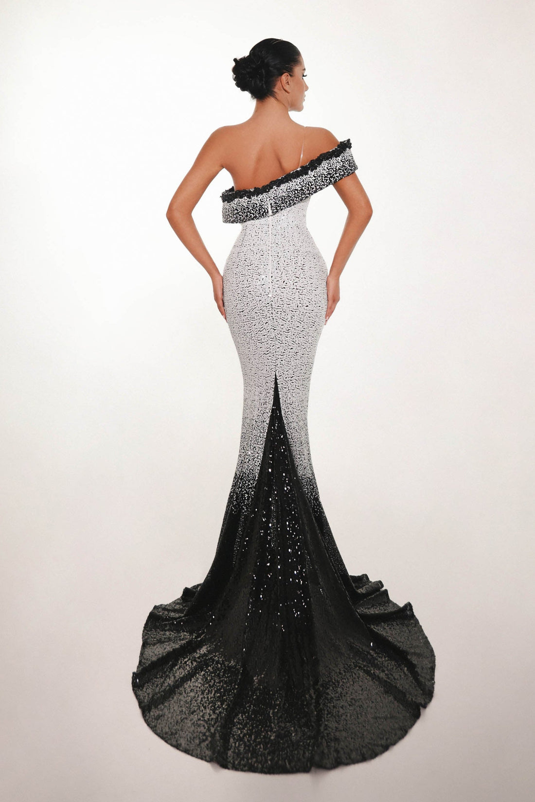 Woman wearing a black and white off-shoulder evening gown with a long train on a light background