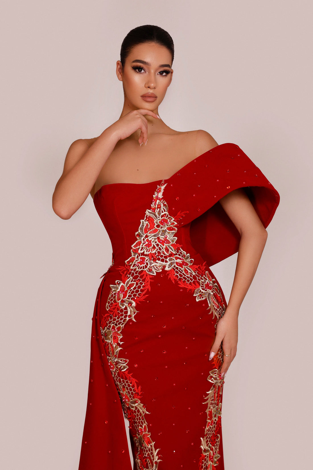 Woman wearing a red evening gown with intricate detailing on a beige background