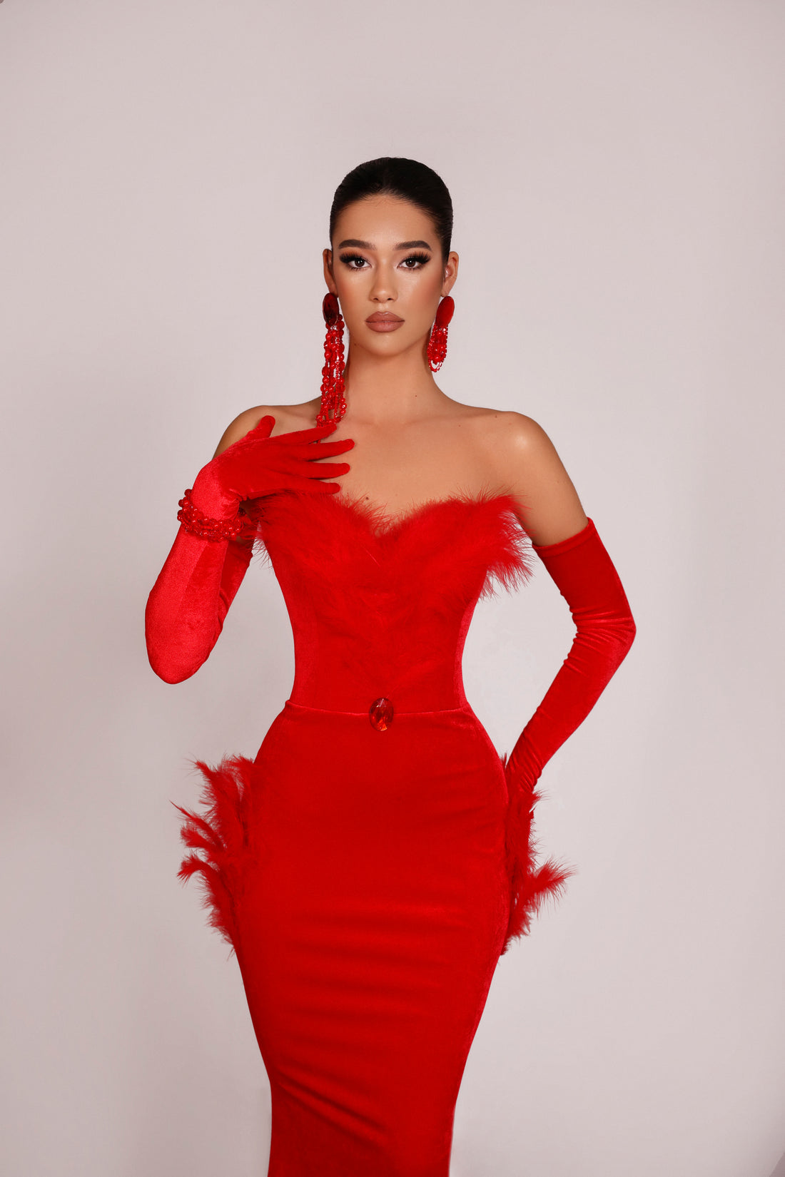Woman wearing a red one-shoulder dress with feather details and long gloves on a plain background
