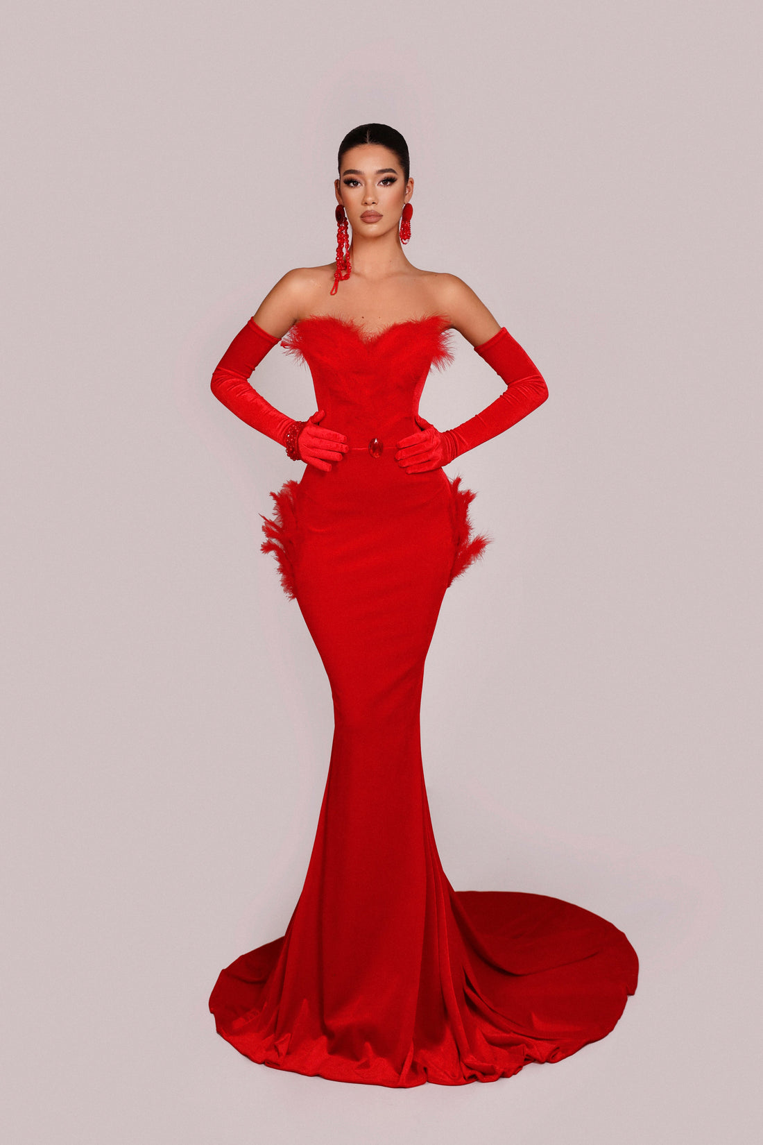 Woman wearing a red evening gown with a fitted bodice and flowing skirt on a light gray background