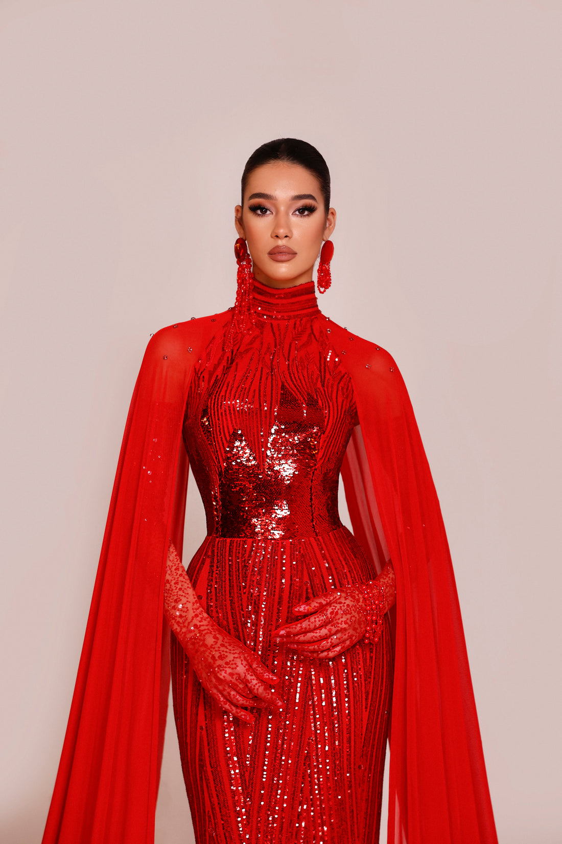 Woman wearing a red sequin dress with a matching cape against a beige background