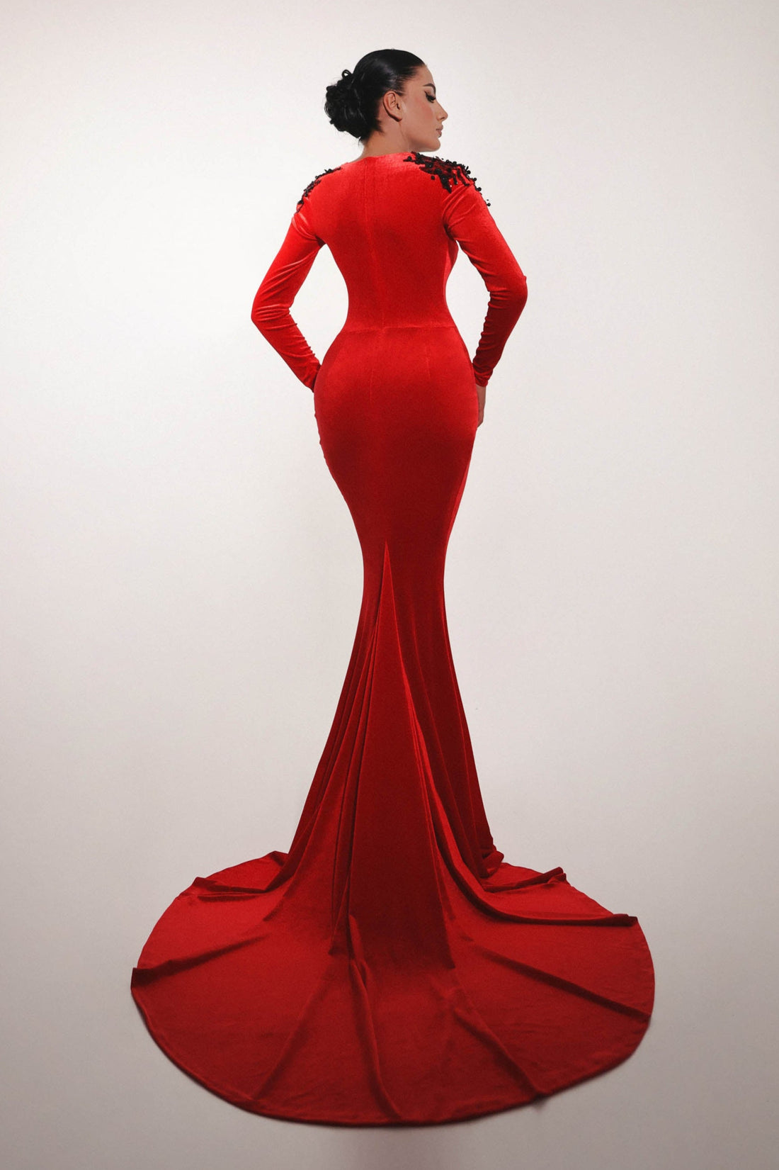 Red evening gown with a long train on a plain background