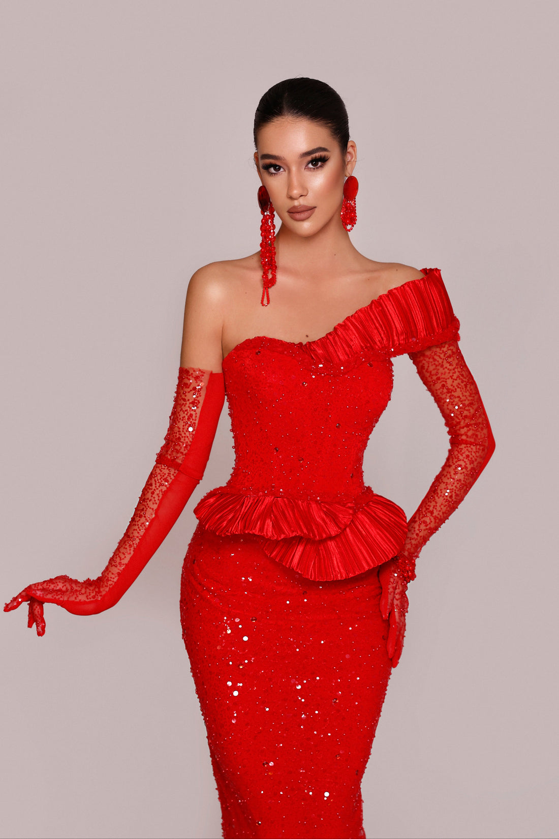 Woman wearing a red one-shoulder dress with matching gloves on a plain background