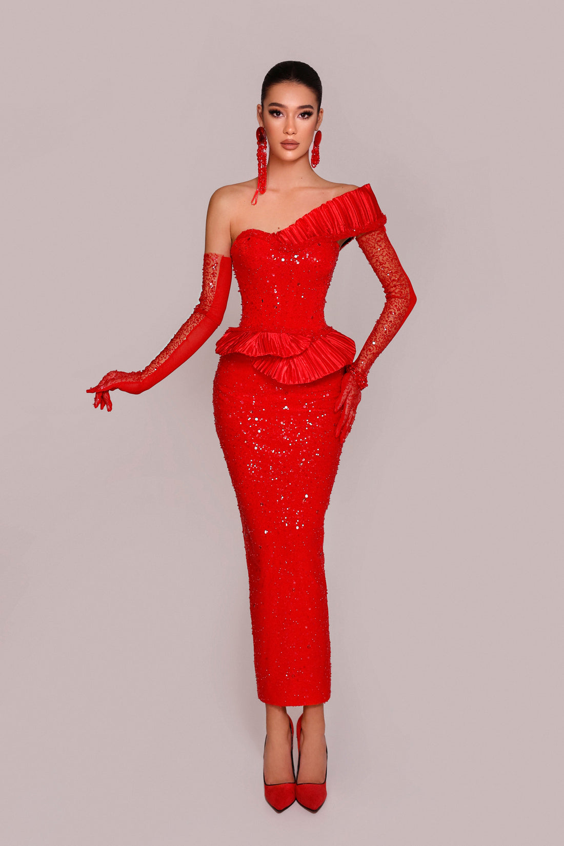 Woman wearing a red one-shoulder dress with long sleeves on a gray background