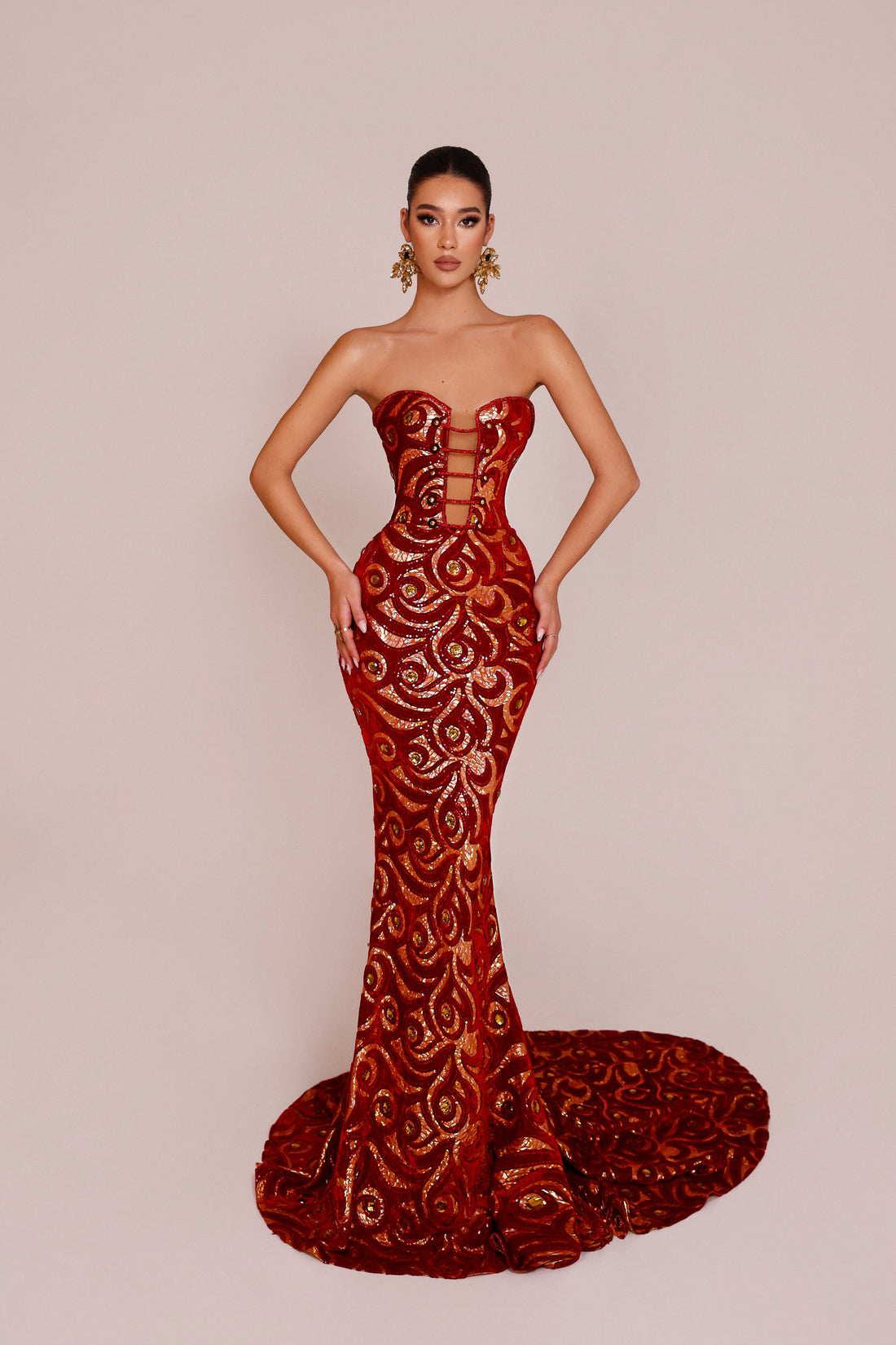 Woman wearing a red strapless gown with intricate lace detailing on a beige background