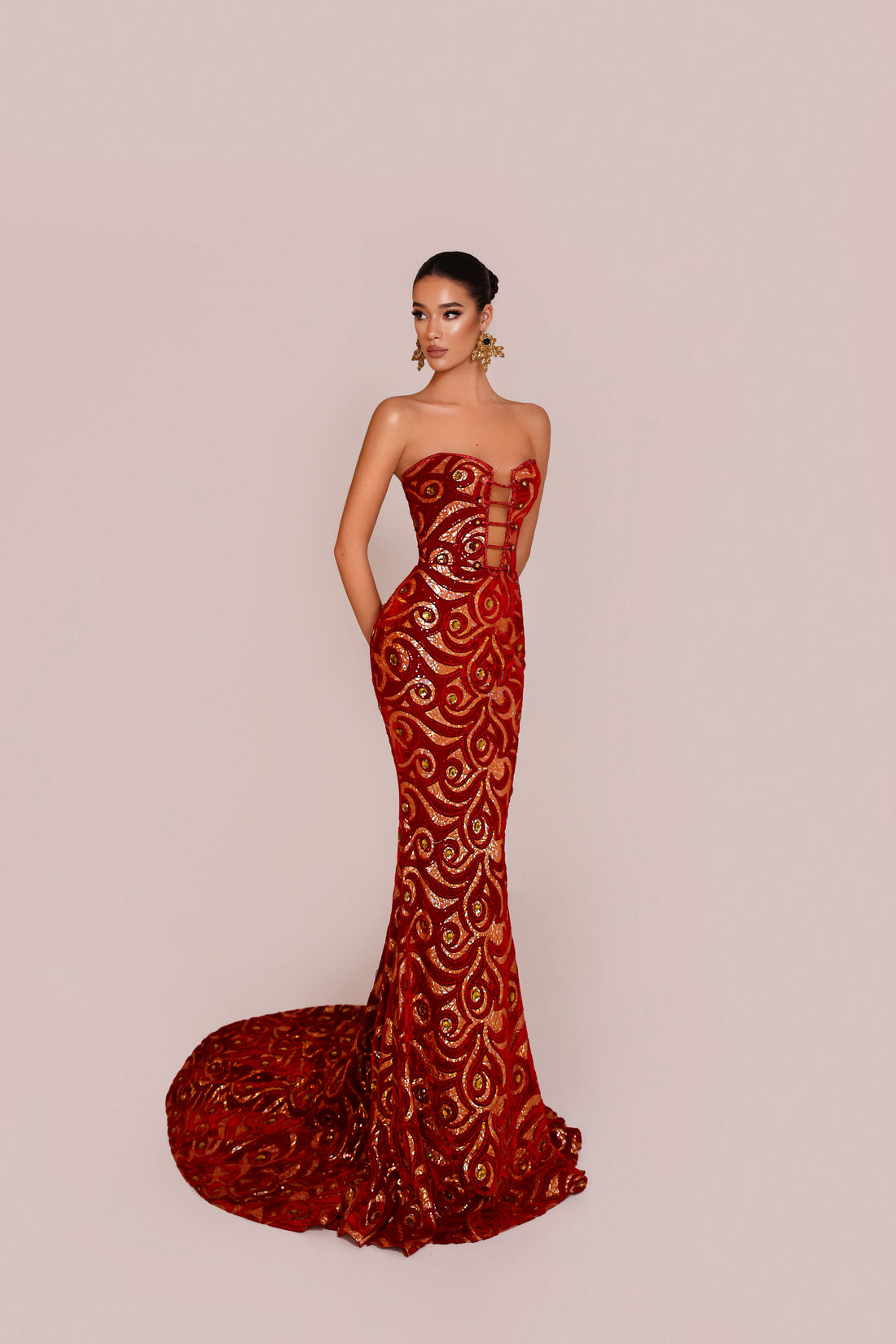 Woman wearing a red strapless gown with intricate detailing on a beige background