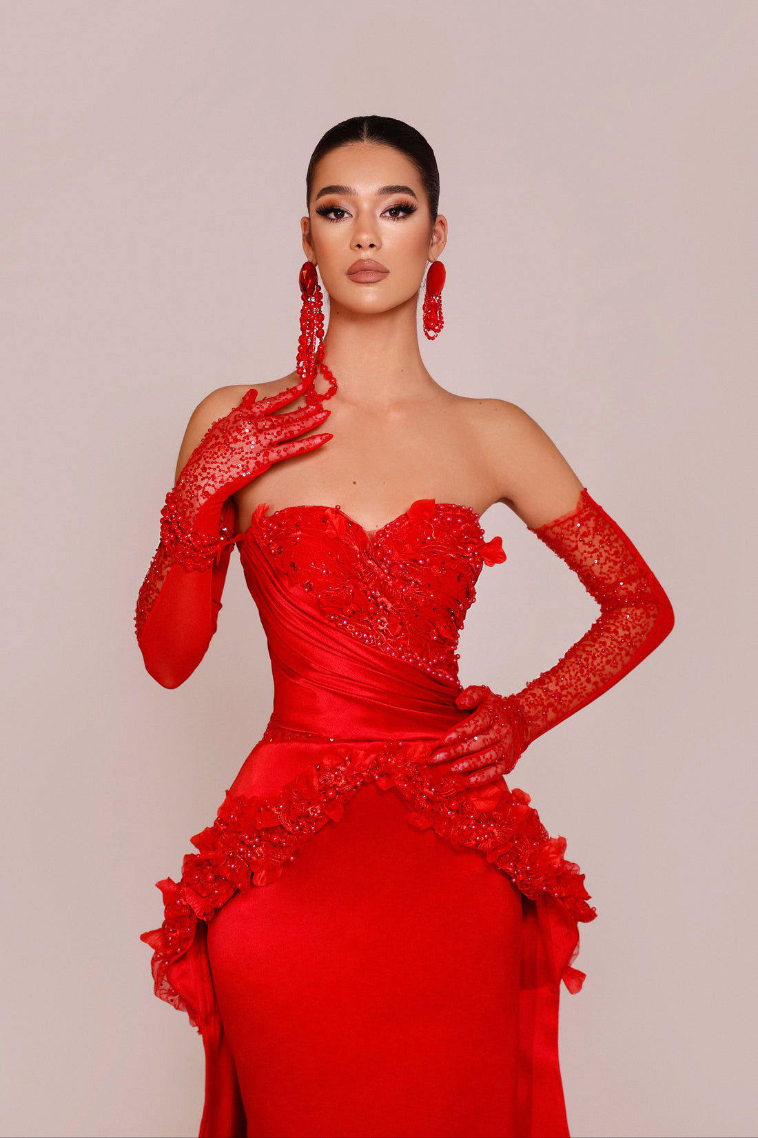 Woman wearing a red evening gown with matching gloves on a beige background