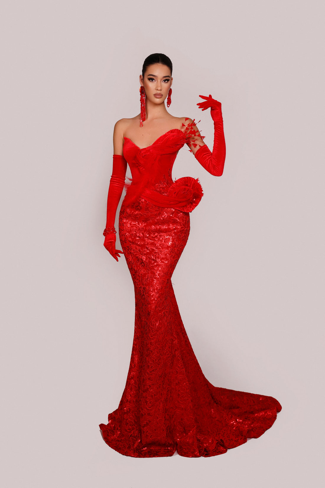 Woman wearing a red evening gown with long gloves on a light gray background